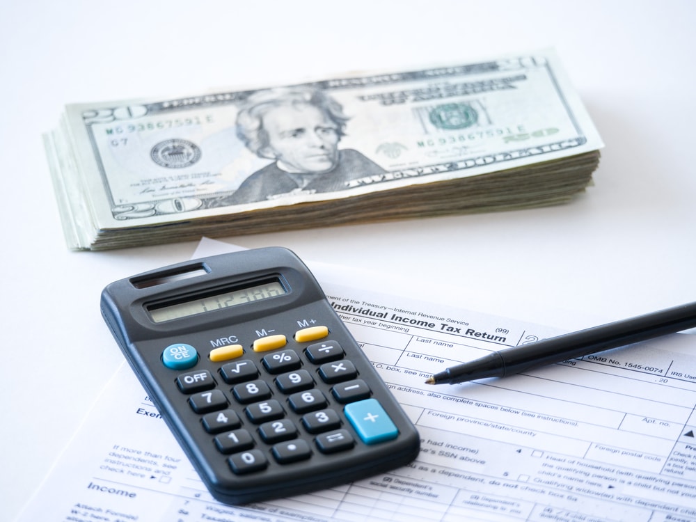 Stack of american money with a calculator over a form